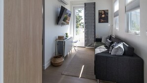 Ein modernes Wohnzimmer mit grauem Sofa, einem flachbildfernseher an der Wand und einem großen Fenster mit Jalousien.