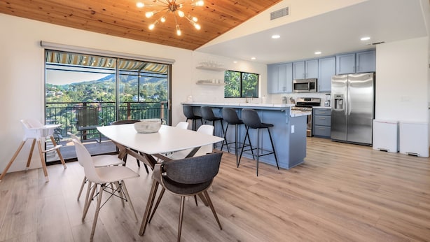 A modern kitchen with a central island, bar stools, and a large window overlooking a scenic view. - Surf Shack at Lake Nacimiento with Private Slip! (Bradley)