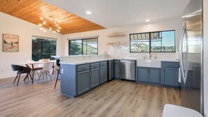 A modern kitchen with wooden ceiling, large windows, and a dining area with chairs. - Surf Shack at Lake Nacimiento with Private Slip! (Bradley)