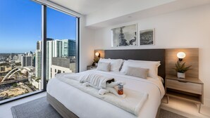 A modern bedroom with a large bed, a nightstand, a wall-mounted lamp, and a view of the cityscape through a large window. - 601 RESIDENCES SKY FLOOR 1BR UNIT #4511 (Miami)