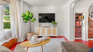 Una sala de estar con televisor, un mueble blanco, piso rojo y una escalera.