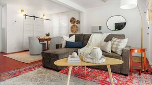 Una sala de estar con un sofá modular, una mesa de centro, un tapete, una mesita auxiliar, una lámpara y un espejo montado en la pared.
