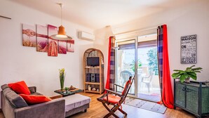 Una sala de estar moderna con un sofá, una silla, un televisor sobre un mueble bajo y un cerramiento de vidrio corredizo que da a un espacio exterior.