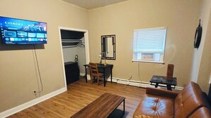 Un salon avec un canapé en cuir marron, une table basse en bois, un téléviseur fixé au mur et une fenêtre avec des stores.