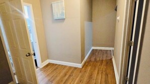 Un couloir doté d’un plancher en bois, de murs de couleur beige et d’un luminaire au plafond.