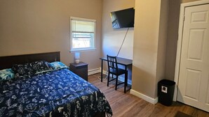 Une chambre à coucher comprenant un lit, un bureau, une chaise, un téléviseur fixé au mur et une porte.