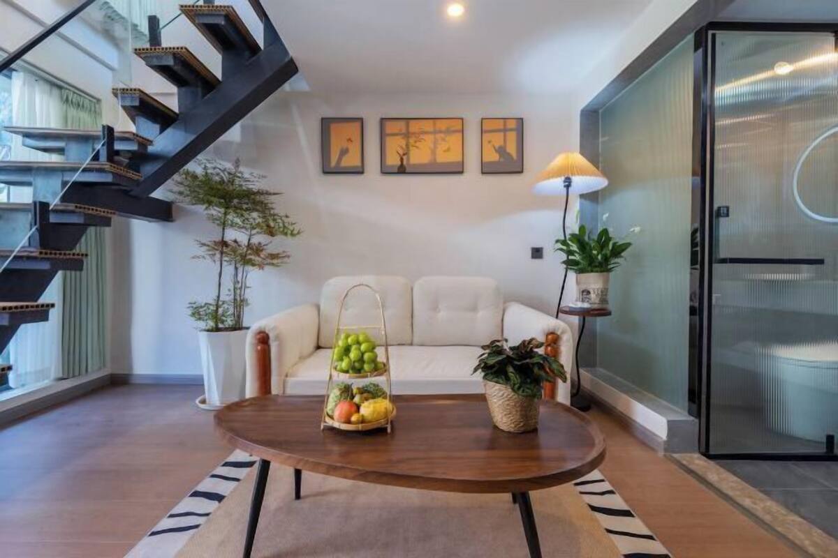 Un salon moderne avec un escalier, un canapé, une table basse sur laquelle on a disposé des fruits, et des œuvres d’art murales.