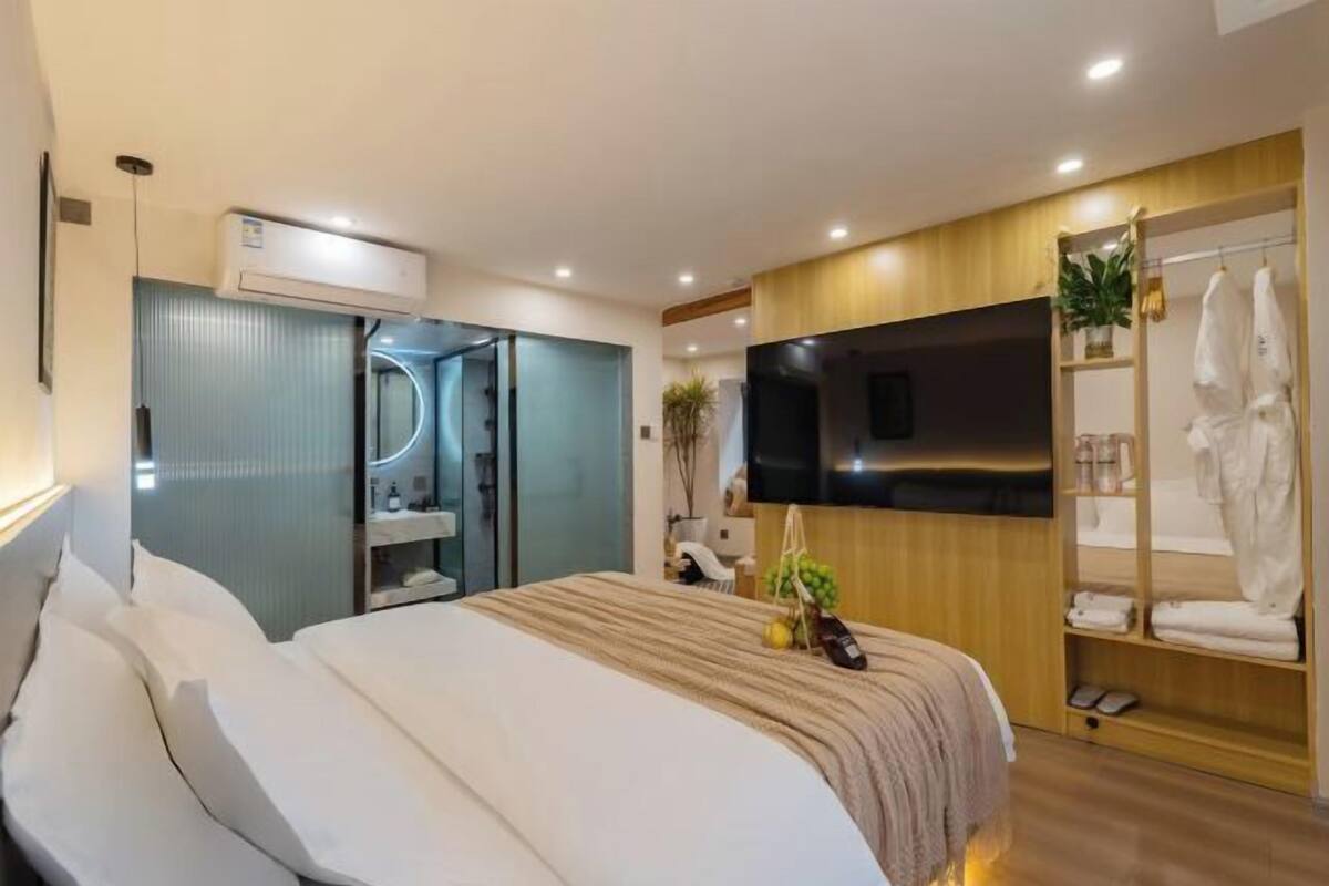Une chambre d’hôtel moderne dotée d’un grand lit, d’un téléviseur fixé au mur, d’une armoire intégrée et d’un petit coin salon.