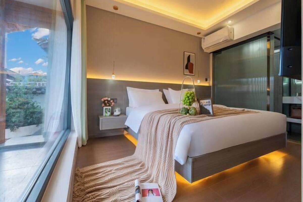 Une chambre à coucher moderne, avec un lit, des tables de chevet, une fenêtre et une vue sur l’extérieur.