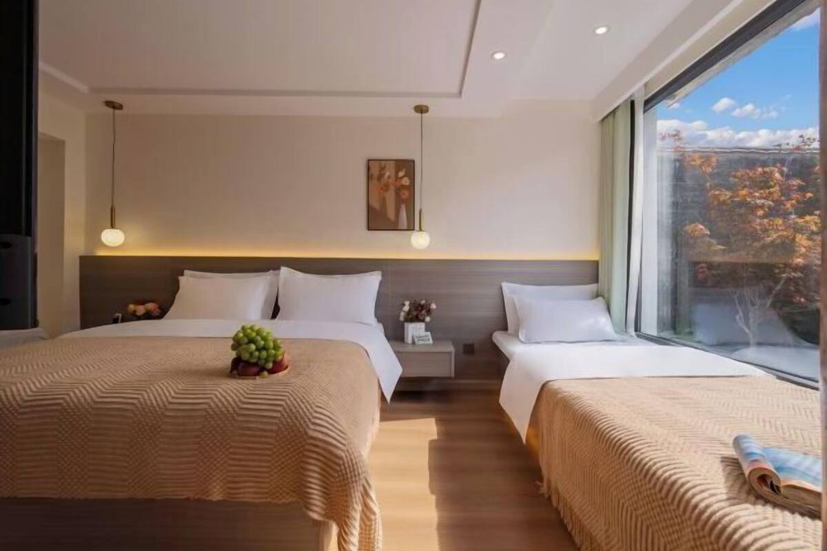 Une chambre d’hôtel moderne avec deux lits, une grande fenêtre donnant sur la verdure et un tableau accroché au mur.