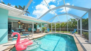 Ein Pool mit einem Flamingo-Schwimmpunkt, umgeben von einer überdachten Terrasse mit Stühlen und einem Tisch.