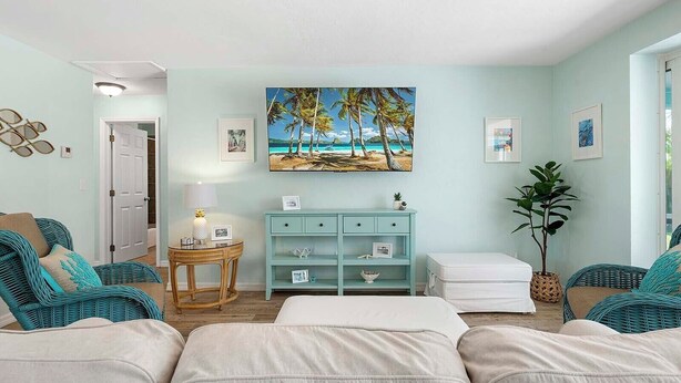 Ein Zimmer mit einem Bett, zwei Korbstühlen, einem kleinen Tisch mit Lampe, einem hellblauen Schrank und einem Bild einer Strandlandschaft.