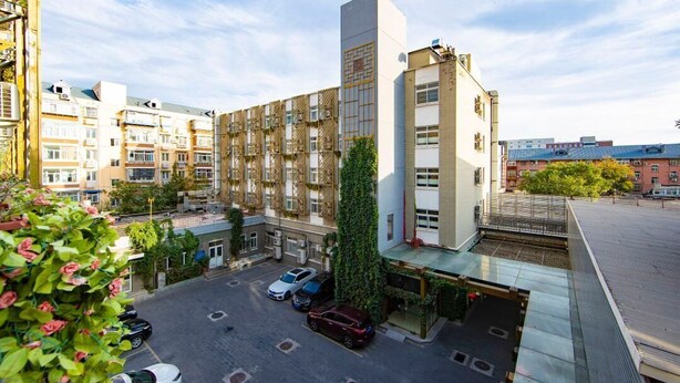 Un hotel a più piani con un cortile centrale, un'area parcheggio e un insieme di edifici residenziali e commerciali sullo sfondo.