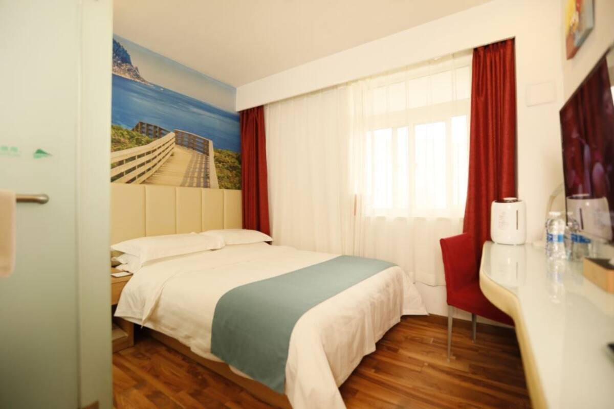 A hotel room with a bed, a desk, a chair, a window with curtains, and a mural on the wall.
