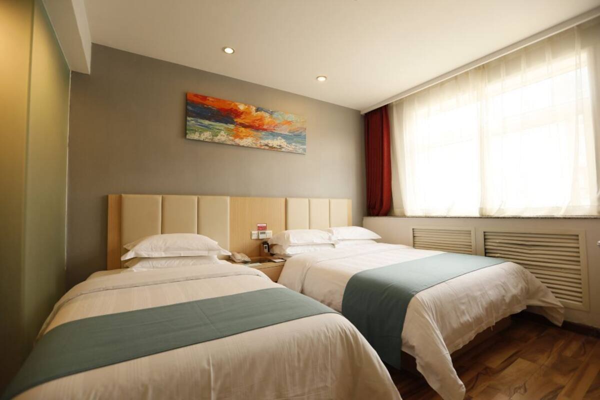 A hotel room with two beds, a painting on the wall, and a window with curtains.