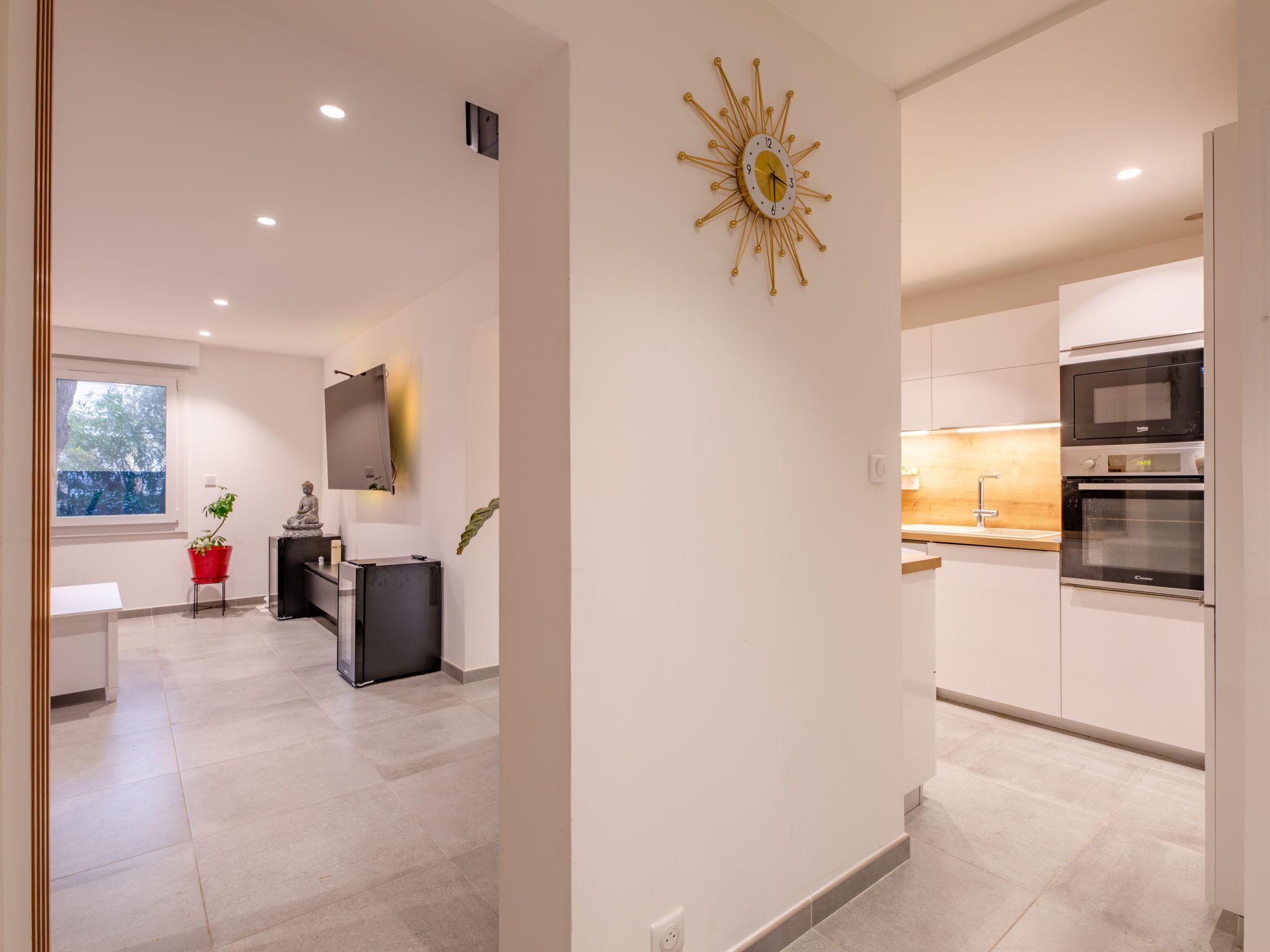 A modern kitchen with built-in appliances, a dining area with a red chair, and a large window.