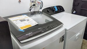 En Whirlpool-tvättmaskin med 17 kg kapacitet, med frontmatning, placerad i ett tvättrum med en dörr och ett vägguttag.