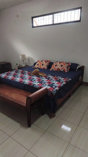 Un dormitorio con una cama, una mesita de noche, una lámpara y una ventana.