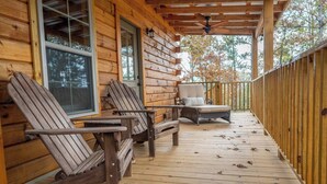 Eine Holzterrasse mit Adirondack-Stühlen und einer Liege, einem Deckenventilator und einem Hollerdungszaun.