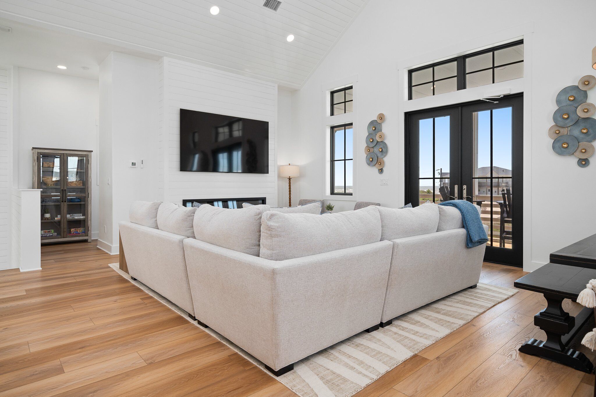 A modern living room with a sectional sofa, a flat-screen TV, and a large window with a view.