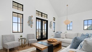 En rummelig stue med en stor sofa, to lænestole, et sofabord og en pejs. Store vinduer og en loftlampe.