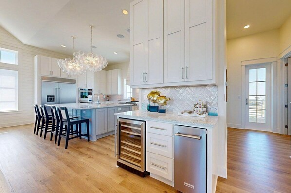 A spacious kitchen with white cabinets, a central island, stainless steel appliances, and a wine cooler.