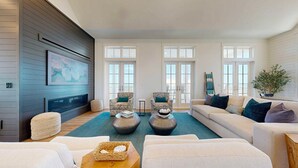 A modern living room with a fireplace, two patterned armchairs, a sofa, and a large window with a view. - Deja View - Ocean Views for Miles with Private Pool, Hot Tub, Game Room & Easy Beach Access (Port Aransas)
