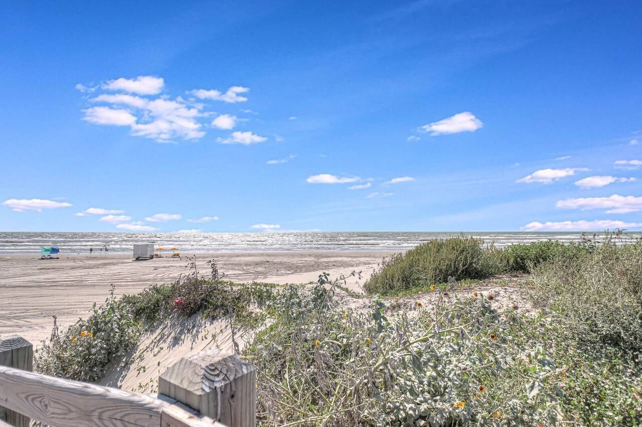 Una playa con una pasarela de madera, dunas arenosas y vegetación escasa.