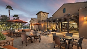 An outdoor patio with seating and tables, a stone building, and a view of the interior dining area.