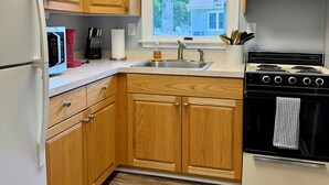 A kitchen with wooden cabinets, a stainless steel sink, a stove, and a refrigerator. - Poseidon’s Mini Getaway: Serene Outer Banks Retreat Near the Beach (Kitty Hawk)