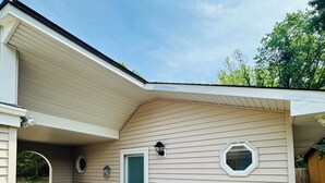 A covered deck with a wooden floor, a small table, and a door leading to a covered porch. - Poseidon’s Mini Getaway: Serene Outer Banks Retreat Near the Beach (Kitty Hawk)
