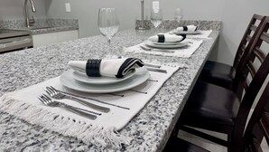 Un coin repas avec une longue table dressée pour quatre personnes, agrémentée d’assiettes blanches, de serviettes pliées et de couverts en argent.