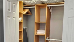 Un dressing accessible sans porte, avec des étagères en bois, une tringle à vêtements et un lit recouvert d’une couvre-lit à motifs.