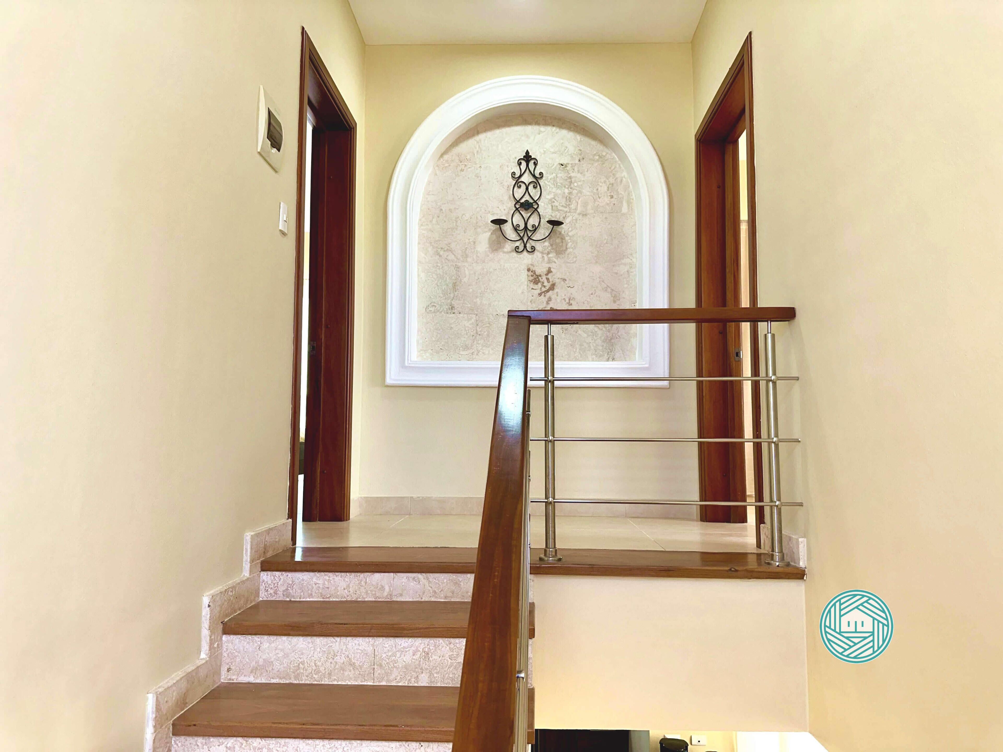 A staircase with wooden steps and a metal handrail, leading to a landing with a decorative wall and a window.