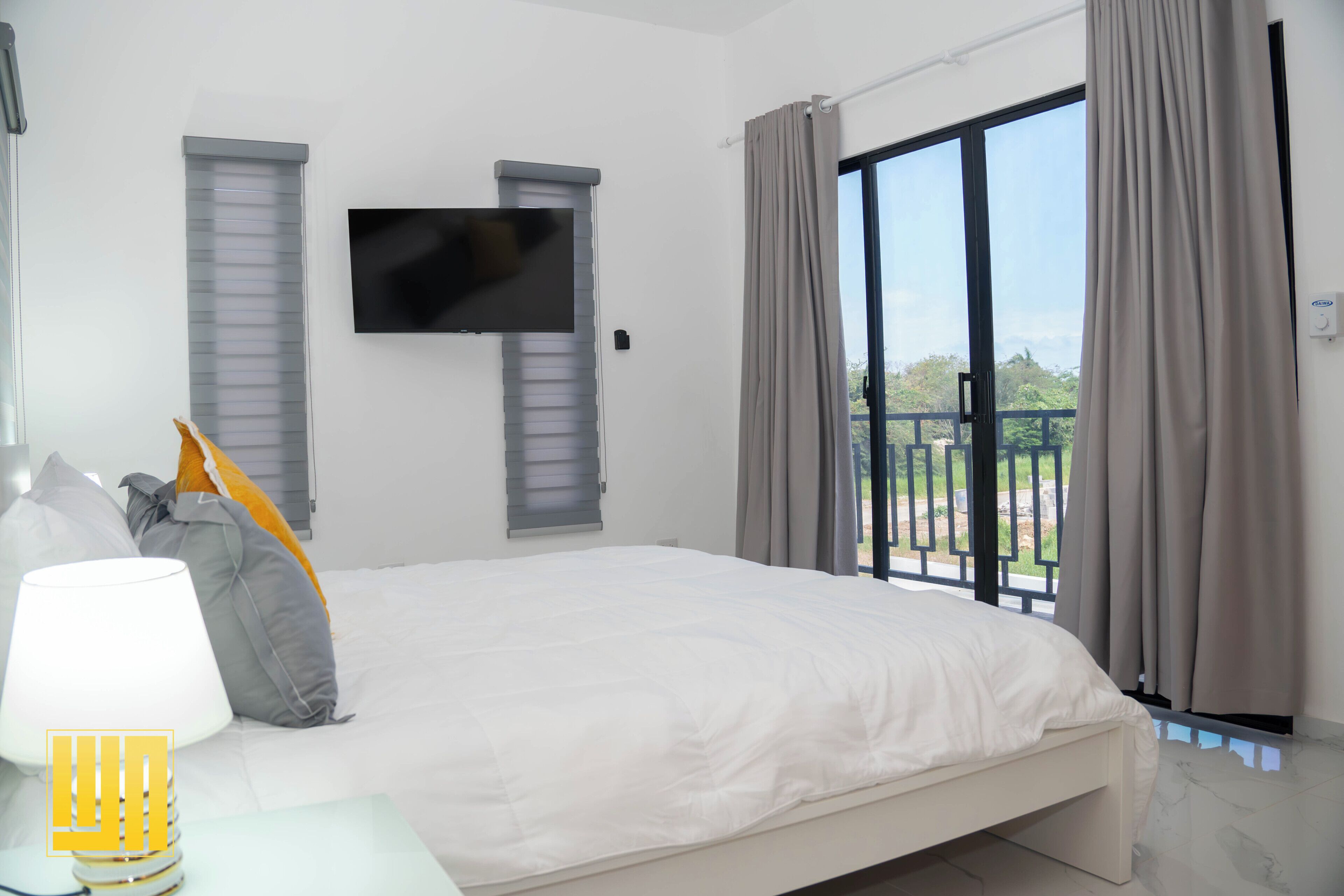 A bedroom with a bed, a flat-screen TV, a window with curtains, and a view of the outdoors.