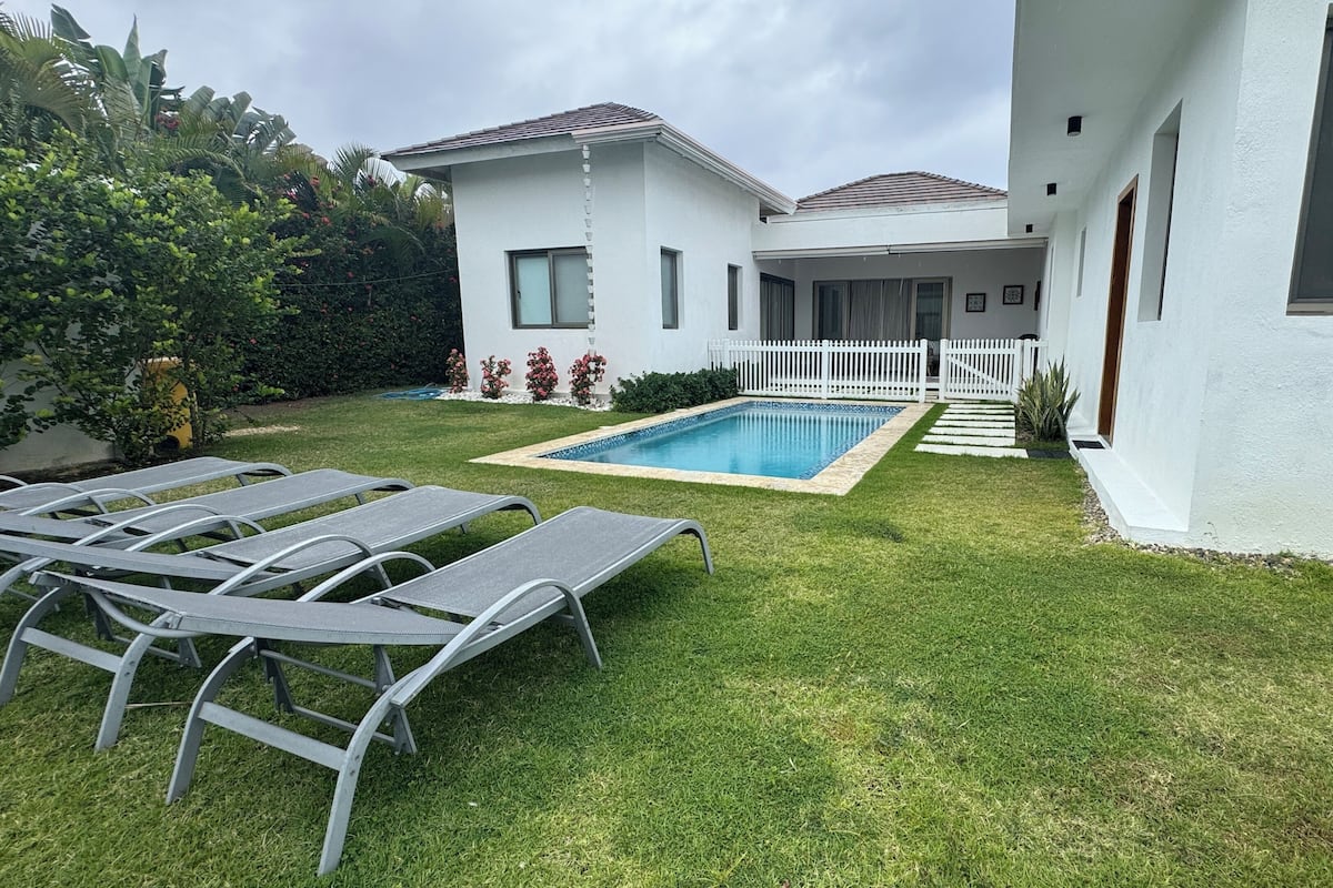 A modern house with a swimming pool, a white fence, and a well-maintained lawn.