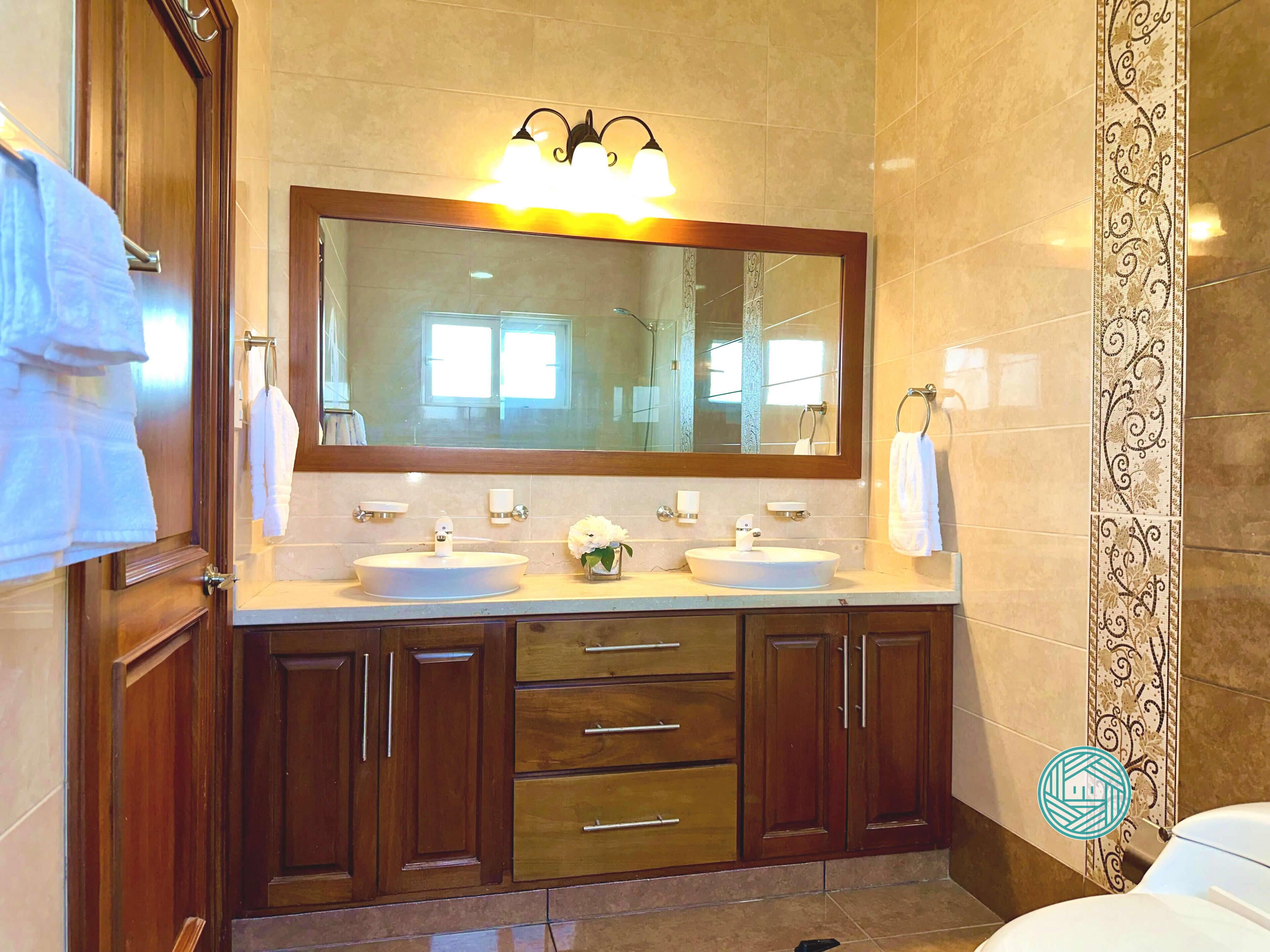 Une salle de bain avec deux lavabos, un grand miroir, des meubles en bois et un porte-serviettes.