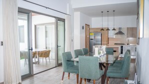 A modern dining area with a glass table and chairs, a kitchen with stainless steel appliances, and a sliding glass door leading to an outdoor area. - Rheia Properties - Sosua Ocean Village (Sosúa)