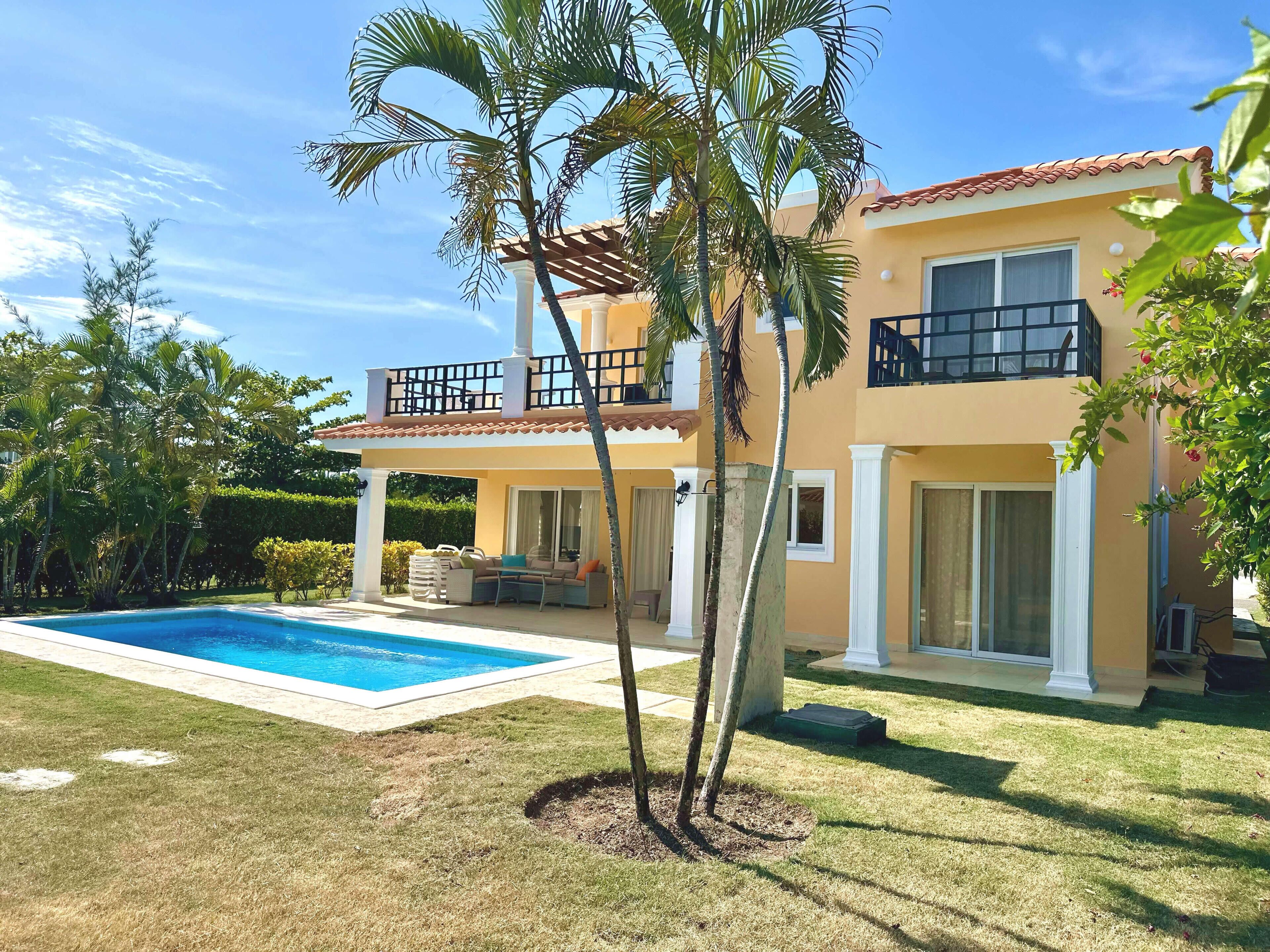Una casa de dos plantas con piscina, un porche cubierto y un césped bien cuidado.