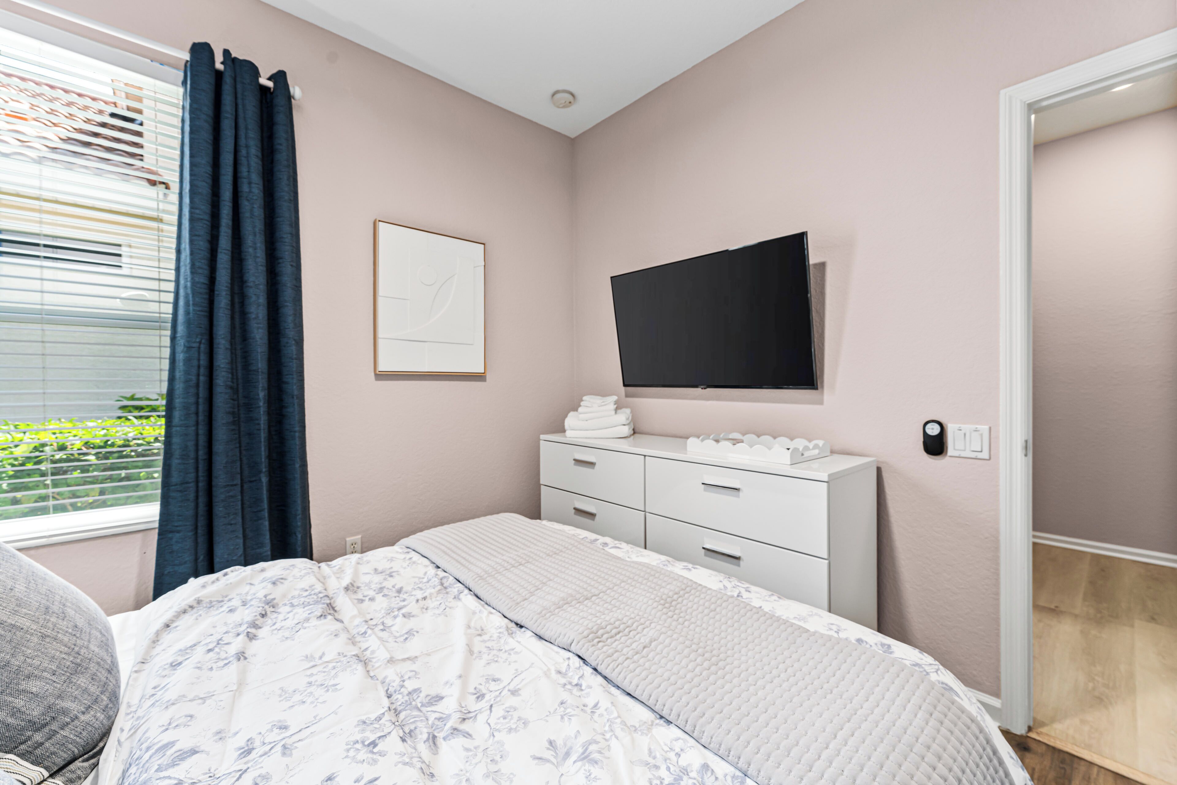 Un dormitorio con cama, cómoda, televisor de pantalla plana y ventana con cortinas.