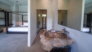 A modern bathroom with a large mirror, a stone sink, and a bed in the adjacent room. - Luxury 4-Bedroom Holiday Rental Near Berawa Beach, Bali Villa 2094 (Bali)