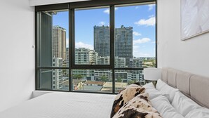 A bedroom with a large window, a bed, and a view of city buildings.