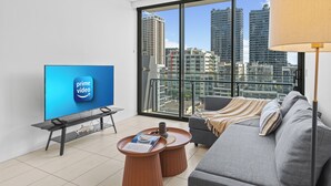 A modern living room with a large TV, a sofa, a coffee table, and a view of tall buildings.