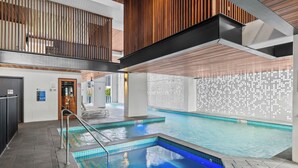 A swimming pool with a blue tint, a wooden ceiling, and a tiled wall with a light pattern.