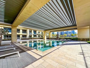 A covered swimming pool area with lounge chairs and a view of the city skyline.