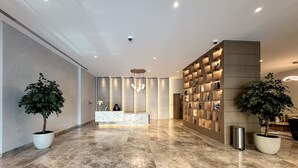 A modern hotel lobby with a reception desk, marble flooring, and two potted plants. - Spectacular Burj View 2BR Luxury (Dubai)
