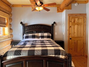 Un dormitorio de estilo cabaña con una cama de madera, un ventilador de techo y una puerta de madera.