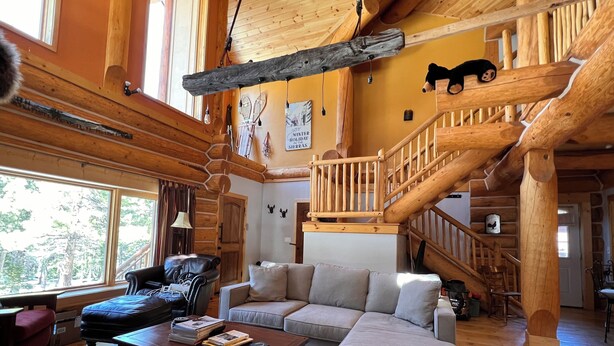 A log cabin interior with a large window, a sofa, a coffee table, and a wooden staircase.