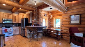 A log cabin kitchen with wooden cabinets, a stone wall, a wooden dining table, and a red chair.