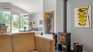 A modern living room with a large window, a sofa, a table with a vase, a fireplace, and a painting on the wall.